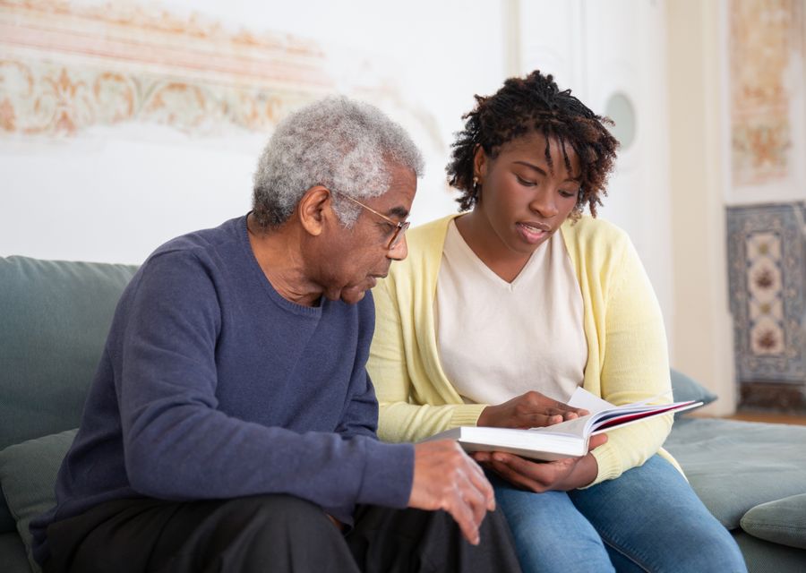 A caregiver reading together with an older man on his couch at home