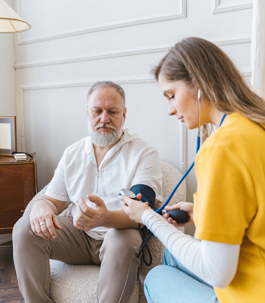 A home health nurse checking an older man's blood pressure in his living room